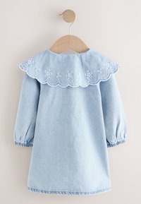 Vaaleansininen farkkukleid, jossa on lehden muotoinen kaulus, valkoista kukkataustaa ja puffihihat. Ripustettu puuhangassa neutraalilla taustalla.