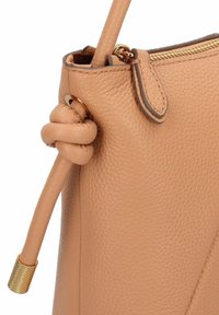Tasche aus braunem Leder mit strukturierter Oberfläche, ausgestattet mit einem geknoteten Trageriemen und einem Reißverschluss in Goldfarbe. Das Design ist kantig mit dezenten Akzenten.