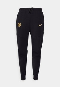 Pantalons de survêtement noirs en mélange de coton, avec un logo Nike doré et un emblème de Chelsea FC. Taille avec cordon de serrage, coupe fuselée, poignets élastiques.