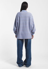 Lange mouwen, lichtblauw shirt met horizontale bruine strepen, relaxed fit en een textuurstof, gedragen met losvallende donkerblauwe jeans.