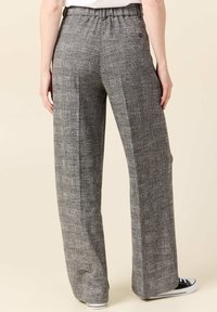 Pantalones de cuadros grises de pierna ancha con una cintura elástica, que cuentan con un bolsillo trasero y una textura suave. Llevados con zapatillas negras.