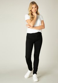 Zwarte slim-fit jeans met een klassiek ontwerp, featuring een middelhoge taille en subtiele stiksels. Gecombineerd met een effen wit t-shirt en witte sneakers.
