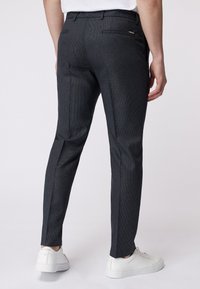 Maßgeschneiderte dunkelgraue Hose aus strukturiertem Stoff, mit schmaler Passform, Gesäßtaschen und kombiniert mit weißen Sneakers.