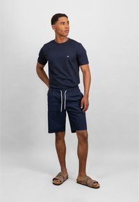 Navy short-sleeve t-shirt with crew neckline and small logo, paired with navy elastic shorts with drawstring and brown slide sandals.