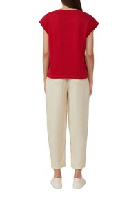Rode t-shirt met korte mouwen en omgeslagen zomen, gecombineerd met wijde crèmekleurige broek. De broek heeft zijzakken en een gladde textuur.