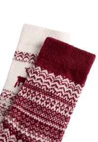 Két kötött téli zokni piros és fehér skandináv mintákkal, az egyik főként fehér piros rénszarvasokkal, a másik piros fehér geometriai mintákkal.