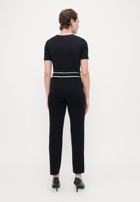 Top negru ajustat cu mâneci scurte, asortat cu pantaloni negri strâmți, având un brâu alb conturat, purtat cu pantofi cu toc negri.