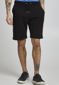 Pantaloni scurți negri din bumbac cu talie elastică și șnur. Include buzunare laterale și un design până la genunchi. Împreună cu adidași negri.