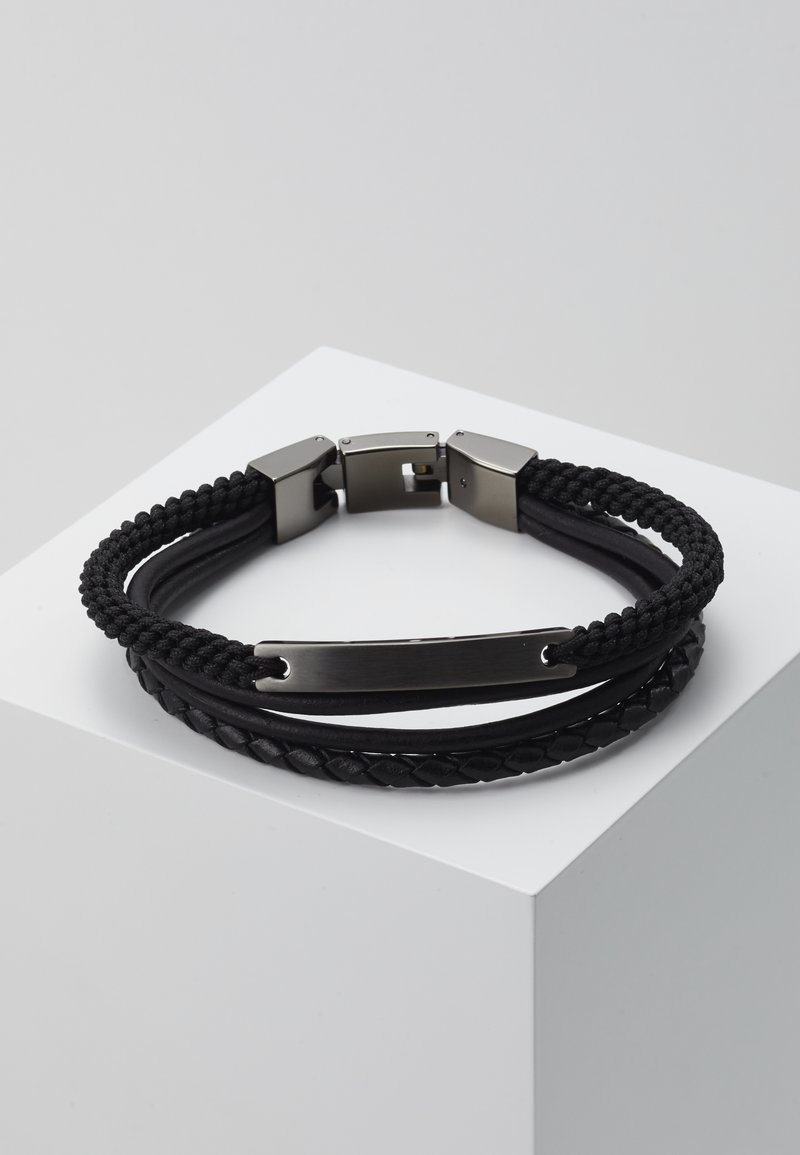 Bracelet noir avec un design tressé, fabriqué en cuir et en cordon, avec un fermoir en métal lisse et une plaque métallique gravée.