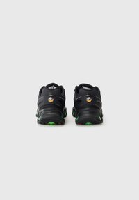 Chaussures de sport noires avec un dessus texturé, des accents réfléchissants et des semelles en caoutchouc vertes et rouges. Conçues pour le confort et la stabilité.