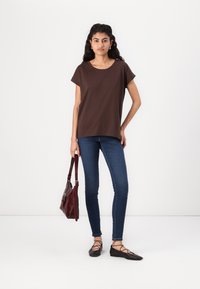 Brown short-sleeve shirt, fitted blue jeans, black flat shoes with crisscross straps, and a burgundy handbag. Simple, casual outfit.