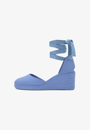 Alpargata azul con cuña, cintas para atar alrededor del tobillo anudadas en lazo, puntera cerrada y suela texturizada.