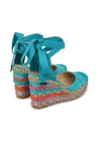 Lanières turquoise en toile avec une plateforme tressée multicolore. Comprend des liens autour de la cheville et un dessus lisse avec des accents texturés.