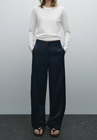 Långärmad vit bomullstop som är matchad med marinblå vida byxor av slätt material, med sidfickor och avslappnad passform.