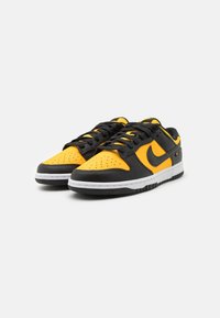 Svarta och gula sneakers med överdel i läder, perforerat tåområde, vit mellansula och svarta snören. Nike-logotyp på sidan.