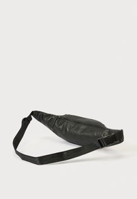 Μαύρο δερμάτινο τσαντάκι μέσης με κεντρικό φερμουάρ και ρυθμιζόμενο μαύρο υφασμάτινο λουράκι με πλαστική πόρπη σε λευκό φόντο.