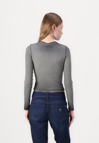 Grå langermet skjorte med ribbet tekstur, tett på kroppen, sammen med mørkeblå jeans med baklommer og subtile detaljer.
