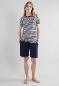 Camisa de rayas en azul marino y blanco combinada con pantalones cortos azul marino. El tejido de algodón es suave, con un escote redondo clásico y bolsillos laterales en los pantalones cortos.