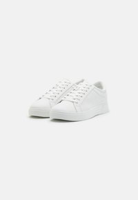 White sneakers with round toe, low top design, smooth leather-like material, flat laces, and textured side panels. Thick rubber sole.