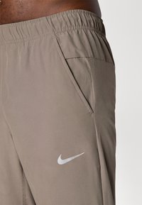 Nike træningsshorts lavet af lysebrunt stof, med en elastisk talje, sidelomme og et sølvfarvet logo.