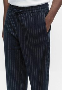 Marinblå randiga byxor gjorda av mjukt tyg, med resårmidja och dragsko samt sidofickor.