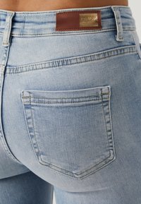 Gros plan de la poche arrière d'un jean en denim bleu clair et de l'étiquette de marque en cuir marron sur la ceinture.