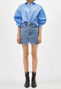 Blå och vit randig skjorta med knappar och puffärmar, i kombination med en fransad denim minikjol och svarta ankelskor.