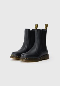 Botas Chelsea pretas em pele com um acabamento texturizado, painéis laterais elásticos e uma alça de puxar com detalhe amarelo. Apresenta uma sola de borracha espessa e durável.