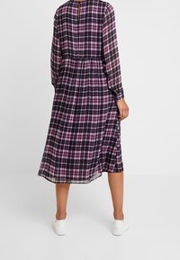 Vestido midi de manga larga en tejido de cuadros púrpura y negro semitransparente, ceñido en la cintura, con un cierre de botones en la parte posterior y una falda fluida.