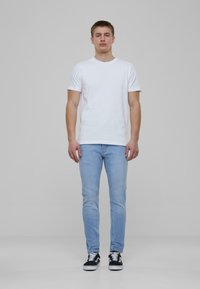 Fehér pamut póló, világoskék slim fit farmernadrág és fekete sportcipő. Az öltözet egyszerű dizájnnal rendelkezik, kerek nyakkivágással és látható minták nélkül.