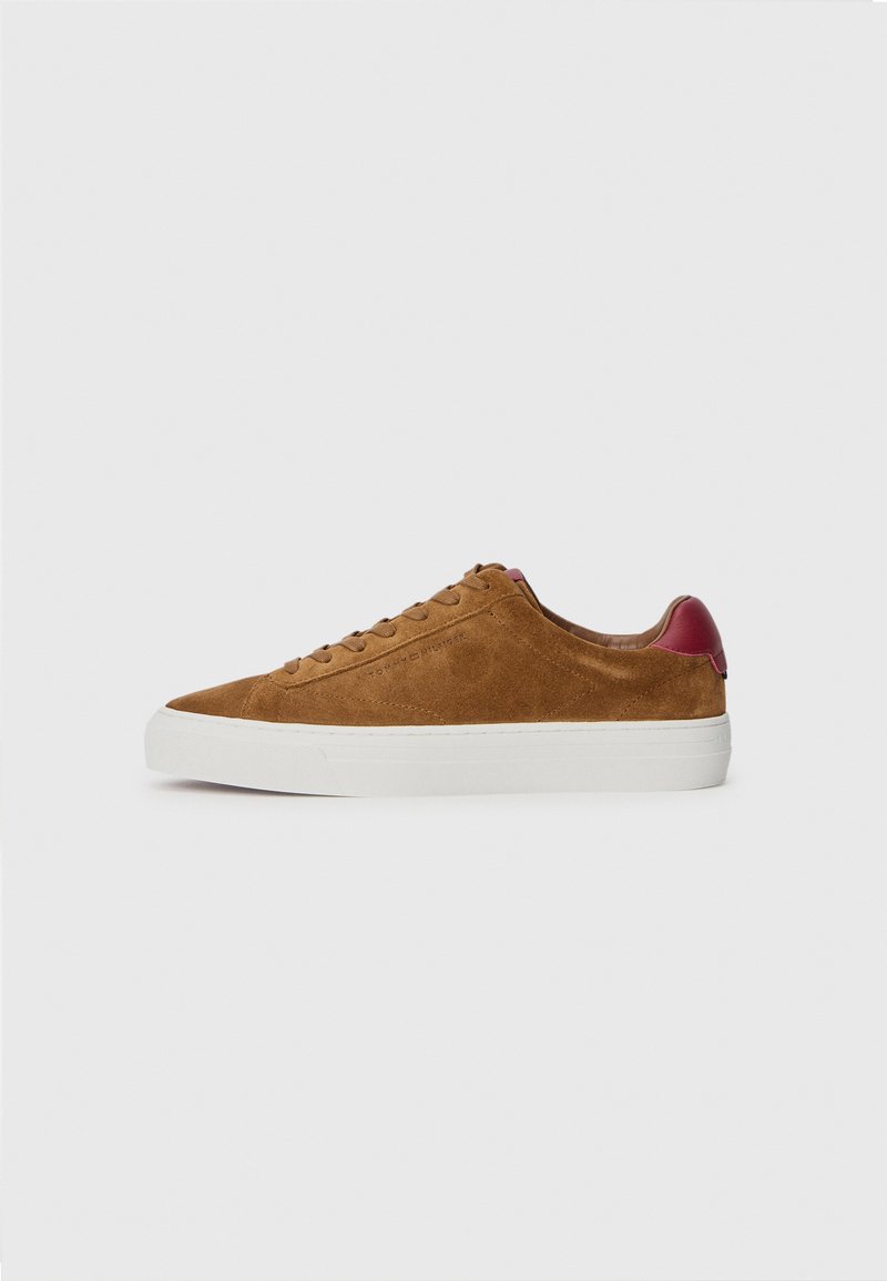Zapatillas de ante marrón con una suela de goma blanca, presentan cordones marrones y un acento burdeos en el talón. Textura suave y diseño aerodinámico.