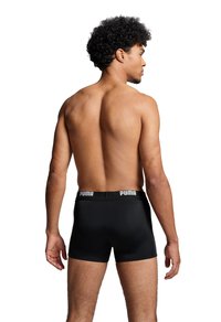 Schwarze Boxershorts mit einem PUMA-Logo am Bund, ausgestattet mit einem figurbetonten Design und einer glatten Textur. Das Modell posiert von hinten.