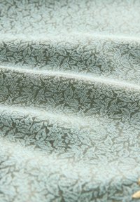 Textil, amely finom levélmintát mutat be világos türkiz és zöld árnyalatokban, puha, textúrált felülettel és lágy redőkkel.