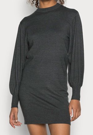Woman wearing a dark gray, long-sleeve knit dress with a ribbed hem, cuffs, and a mock neck, standing against a plain background.