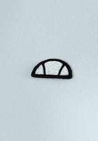 Logotipo bordado en blanco y negro con forma semicircular sobre un fondo de tela gris claro. El logotipo presenta tres secciones sombreadas en blanco.