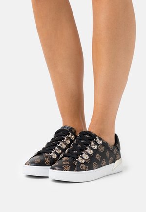 Las zapatillas negras tienen un material superior texturizado con un patrón dorado, ojales plateados y una suela de goma blanca. El diseño es de tipo bajo con cordones.