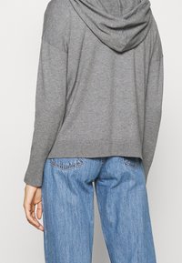 Sweat à capuche gris avec une coupe décontractée, ourlet côtelé et texture douce, associé à un jean droit bleu clair.