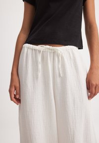 Valged puuvillased püksid, millel on tekstureeritud, kortsuline välimus; omad elastse vöökoha, millel on ees lipsustatud nöör.