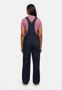 Denim overalls in dark blue with a relaxed fit, featuring adjustable straps, front and back pockets, and contrasting orange stitching.