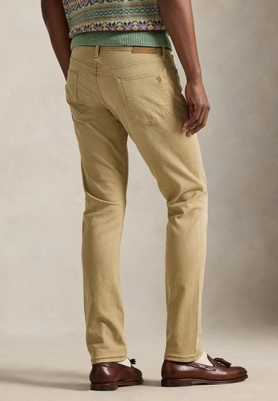 Calças chino bege feitas de algodão, com corte slim, bolsos traseiros e detalhe do logotipo. Estilizadas com mocassins castanhos e um suéter estampado.