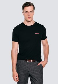 Černé tričko s krátkým rukávem a kulatým výstřihem, s červeným potiskem slova "merry." na levé straně hrudi, spárované se šedými kostkovanými kalhotami.