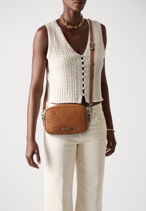 Brun läder crossbody-väska med präglat mönster, rektangulär form, justerbar rem och silverfärgad hårdvara. Bärs över beige byxor.