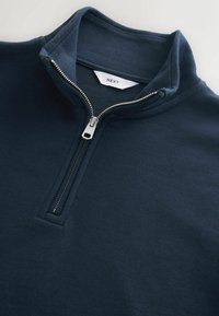 Pull-over marine à fermeture éclair quart, avec une fermeture éclair argentée et un col montant, montrant l'étiquette de marque blanche "NEXT" à l'intérieur de la nuque.