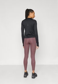 Μαύρο αθλητικό τοπ με μακριά μανίκια σε συνδυασμό με μπορντό κολάν, με επίπεδες ραφές, εφαρμοστή σχεδίαση και αντανάκλαστικές λεπτομέρειες. Φορεμένο με μαύρα αθλητικά παπούτσια.