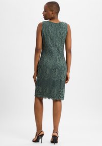 Groene kant jurk met bloemenpatroon, mouwloos ontwerp en aansluitende silhouet. Beschikt over een rits aan de achterkant en een gegolfde zoom.