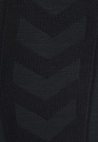 Zwart textiel met een gestructureerd oppervlak, versierd met een patroon van chevronvormen, wat visueel contrasteert met het ribbelachtige oppervlak.