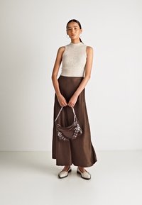 Top sans manches côtelé crème, jupe maxi marron, sac marron à motifs et chaussures crème avec des accents. Ensemble simple et élégant sur un fond neutre.