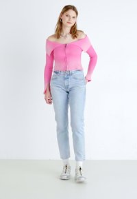Suéter corto de canalé rosa, con cuello off-shoulder y mangas largas, combinado con jeans de tiro alto azul claro y zapatillas grises. Un look simple y a la moda.