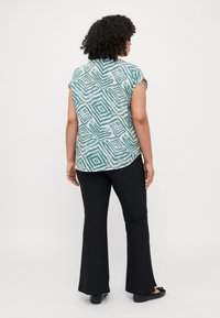 Short-sleeved top in teal with a geometric pattern, paired with black flared pants and black flats. The top is loose-fitting and lightweight.