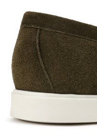 Zielone zamszowe trampki w kolorze oliwkowym, z zaokrąglonym obcasem, białą gumową podeszwą i widocznymi szwami wzdłuż szwów. Teksturowana powierzchnia na całej długości.
